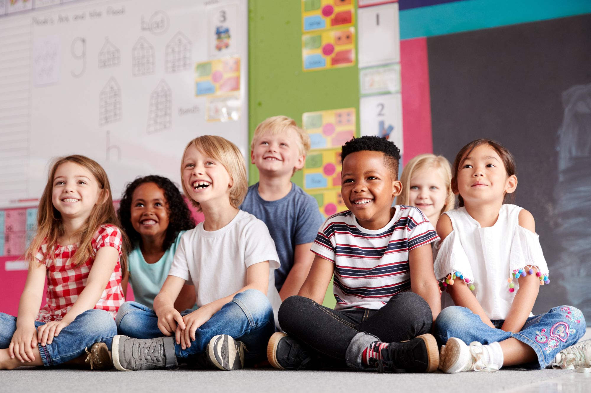 Diverse kids sitting on the floor cross legged in a classroom.